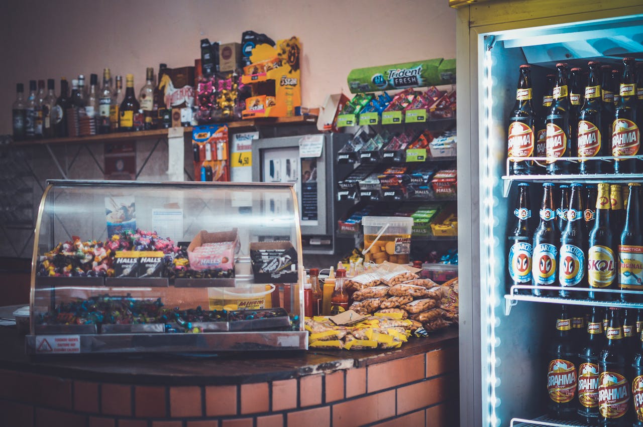Services-01 A well-stocked convenience store counter with snacks, drinks, and a refrigerator showcasing beverages.